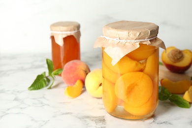 Photo of Glass jar of pickled peaches and fresh fruits on white marble table. Space for text