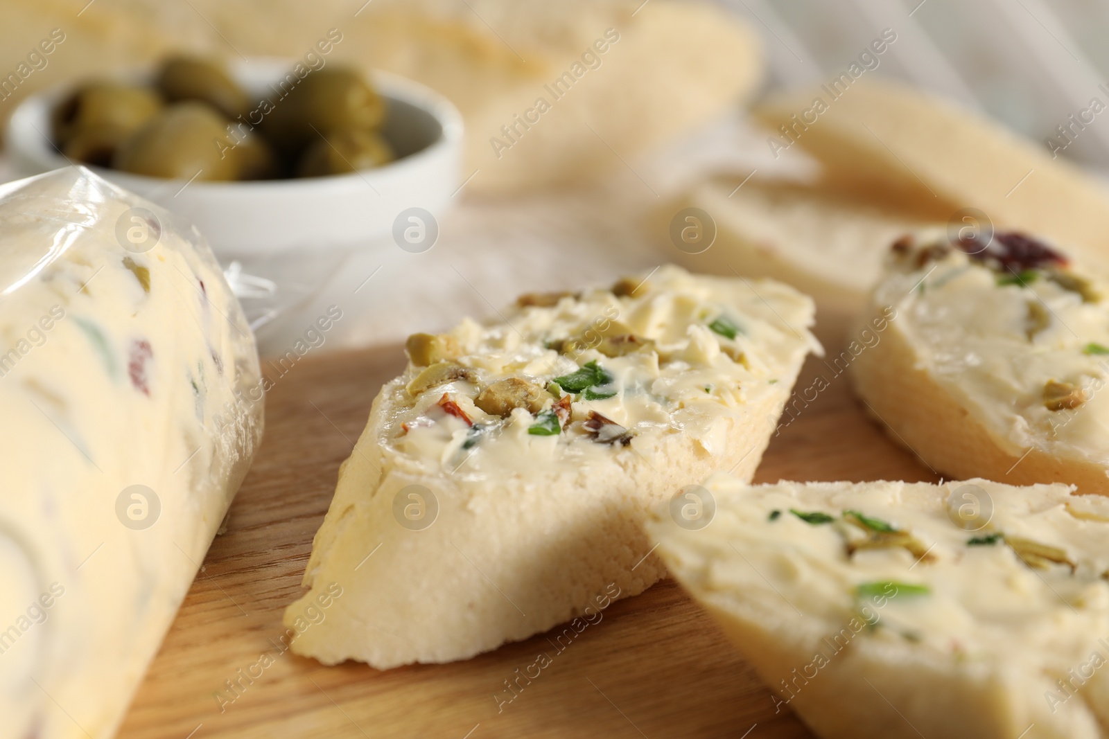 Photo of Tasty butter with olives, green onion and bread on wooden board, closeup