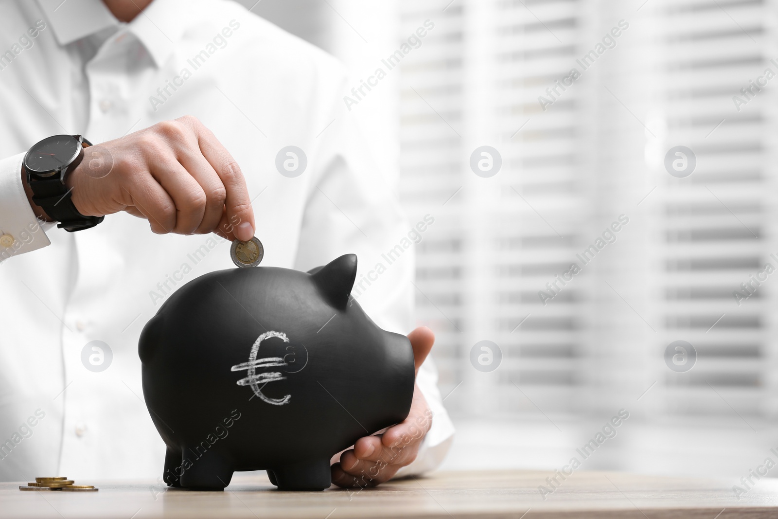 Photo of Man putting coin into piggy bank with euro sign at wooden table, closeup. Space for text