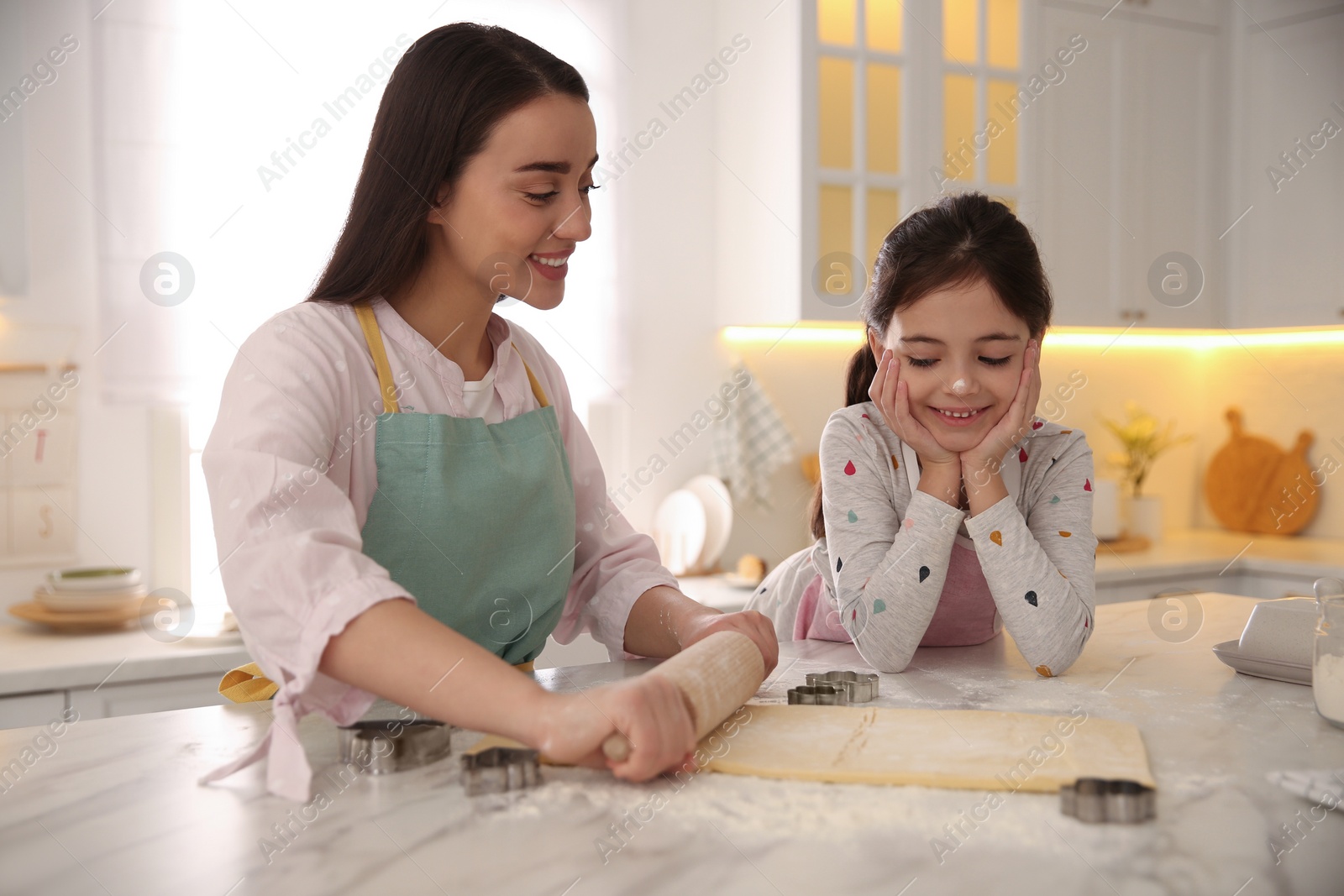 Photo of Mother with her cute little daughter rolling dough in kitchen