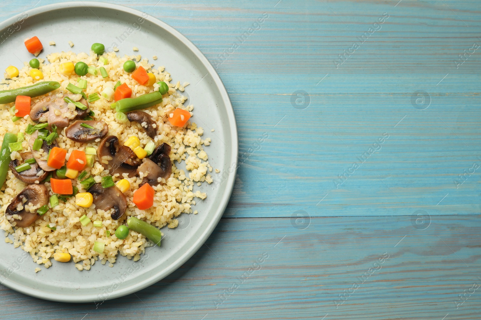 Photo of Delicious bulgur with vegetables and mushrooms on light blue wooden table, top view. Space for text