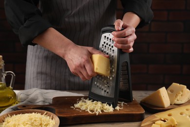 Woman grating cheese at wooden table, closeup