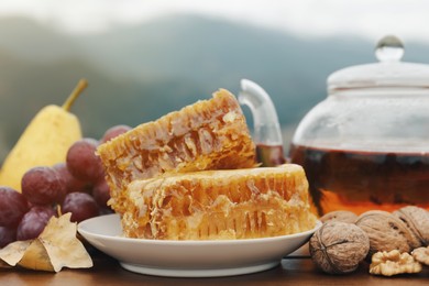 Photo of Tasty fresh honeycombs, fruits, walnuts and aromatic tea on wooden table outdoors, closeup