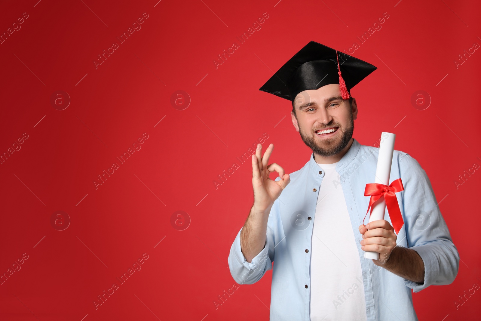 Photo of Happy student with graduation hat and diploma on red background. Space for text