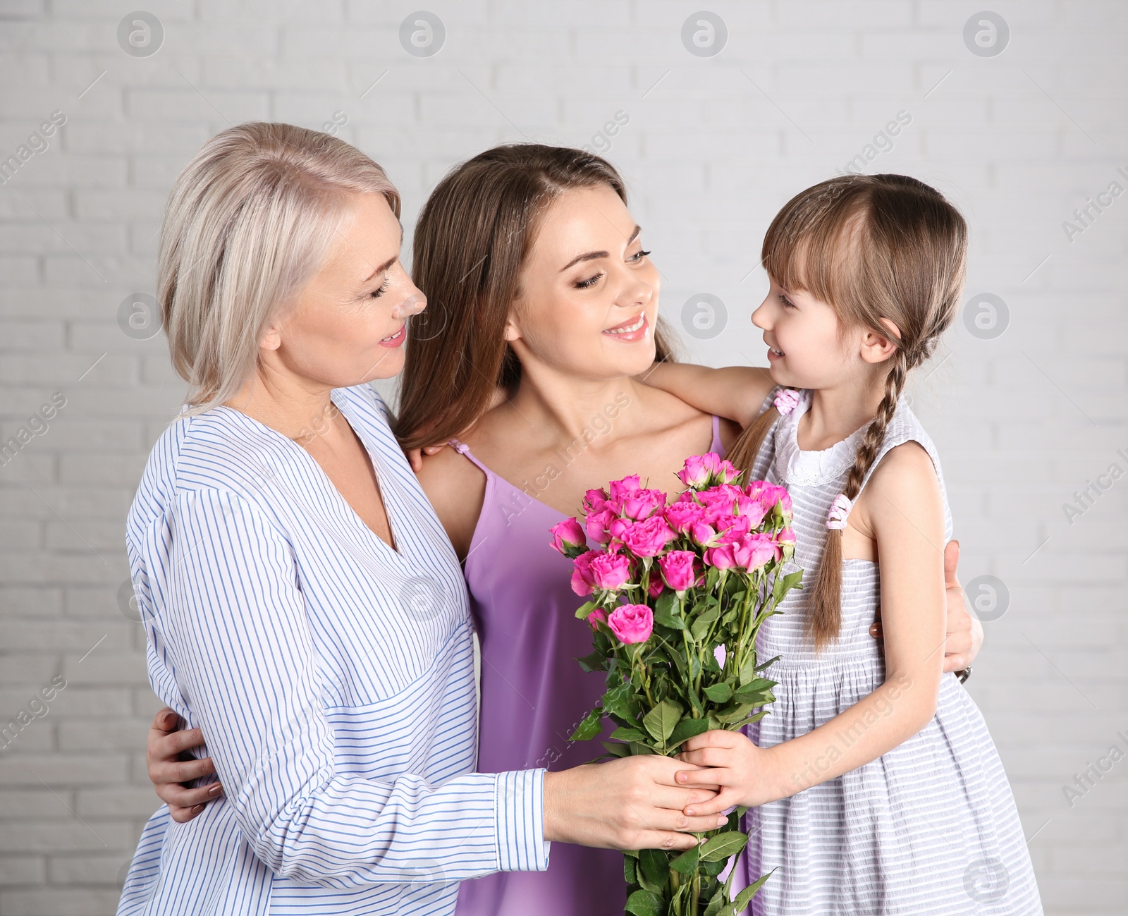 Photo of Beautiful mature lady, daughter and grandchild with flowers near brick wall. Happy Women's Day