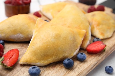 Photo of Wooden board with delicious samosas and berries on light table, closeup