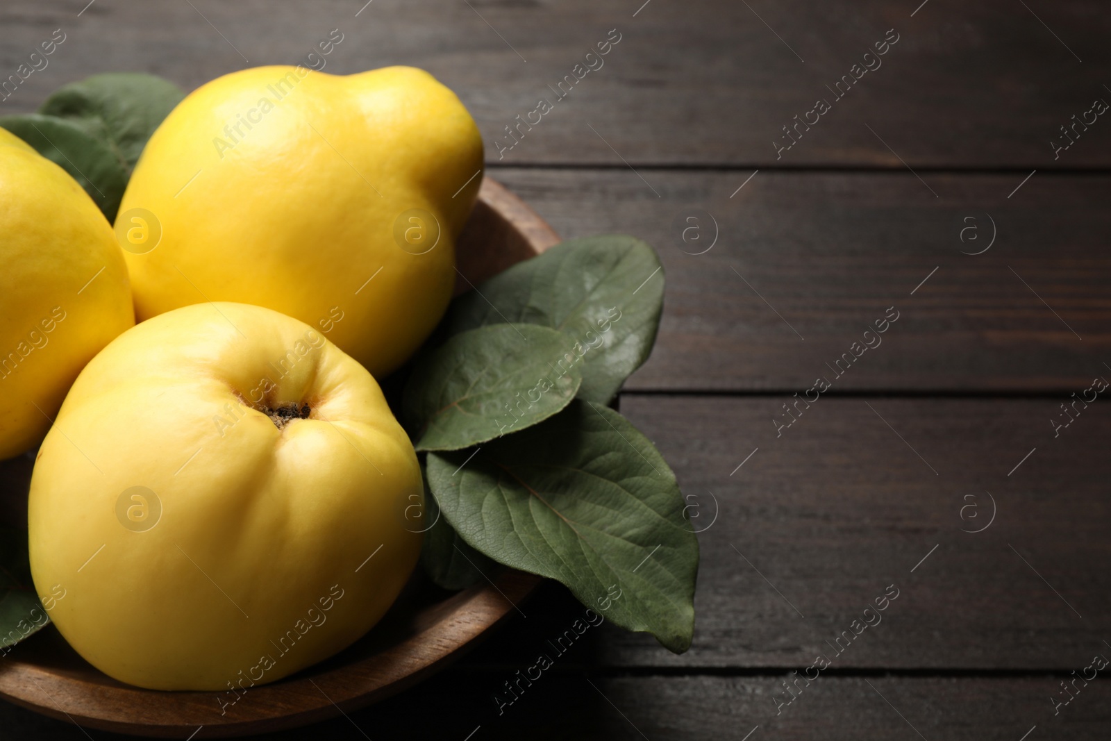 Photo of Fresh ripe organic quinces with leaves on wooden table, closeup. Space for text