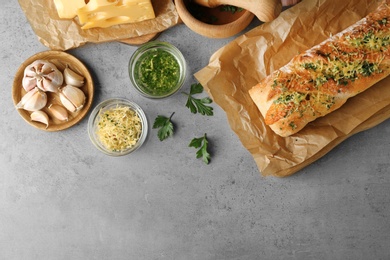 Photo of Tasty homemade garlic bread with cheese and herbs on grey table, flat lay. Space for text