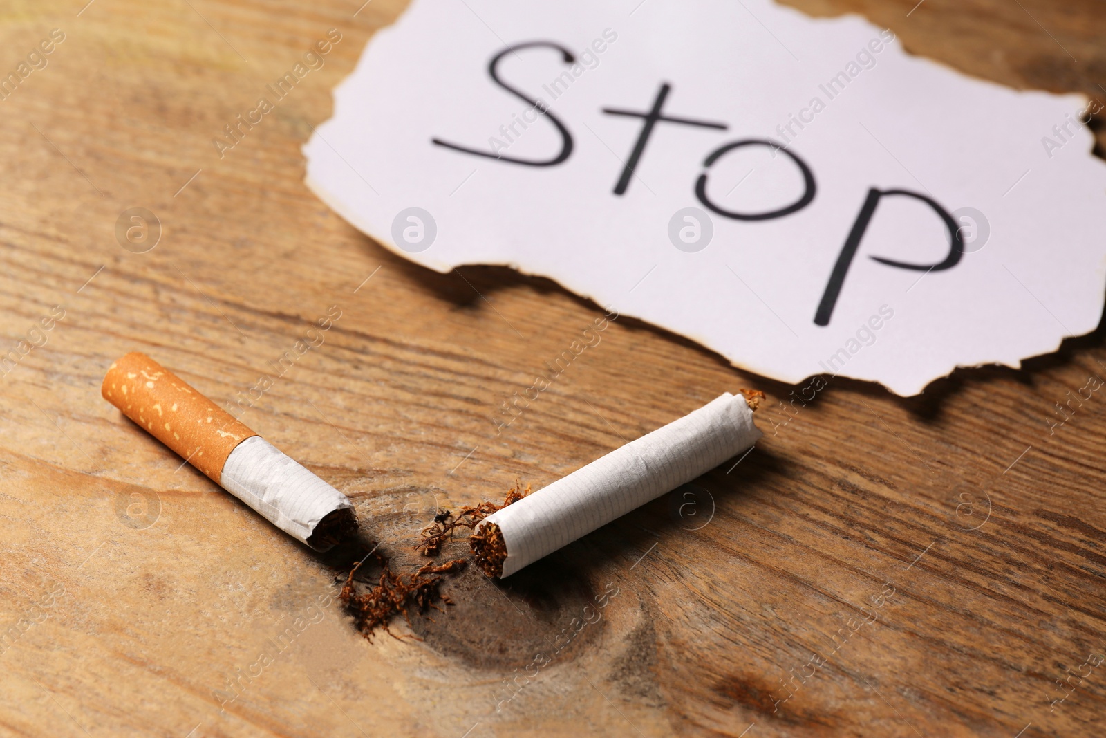 Photo of Broken cigarette and word Stop written on paper on wooden table, closeup. No smoking concept