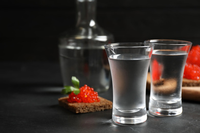 Photo of Cold Russian vodka and sandwiches with red caviar on black table, closeup