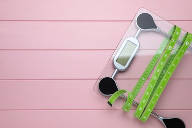 Photo of Bathroom scale, measuring tape and space for text on pink wooden floor, top view. Weight loss concept