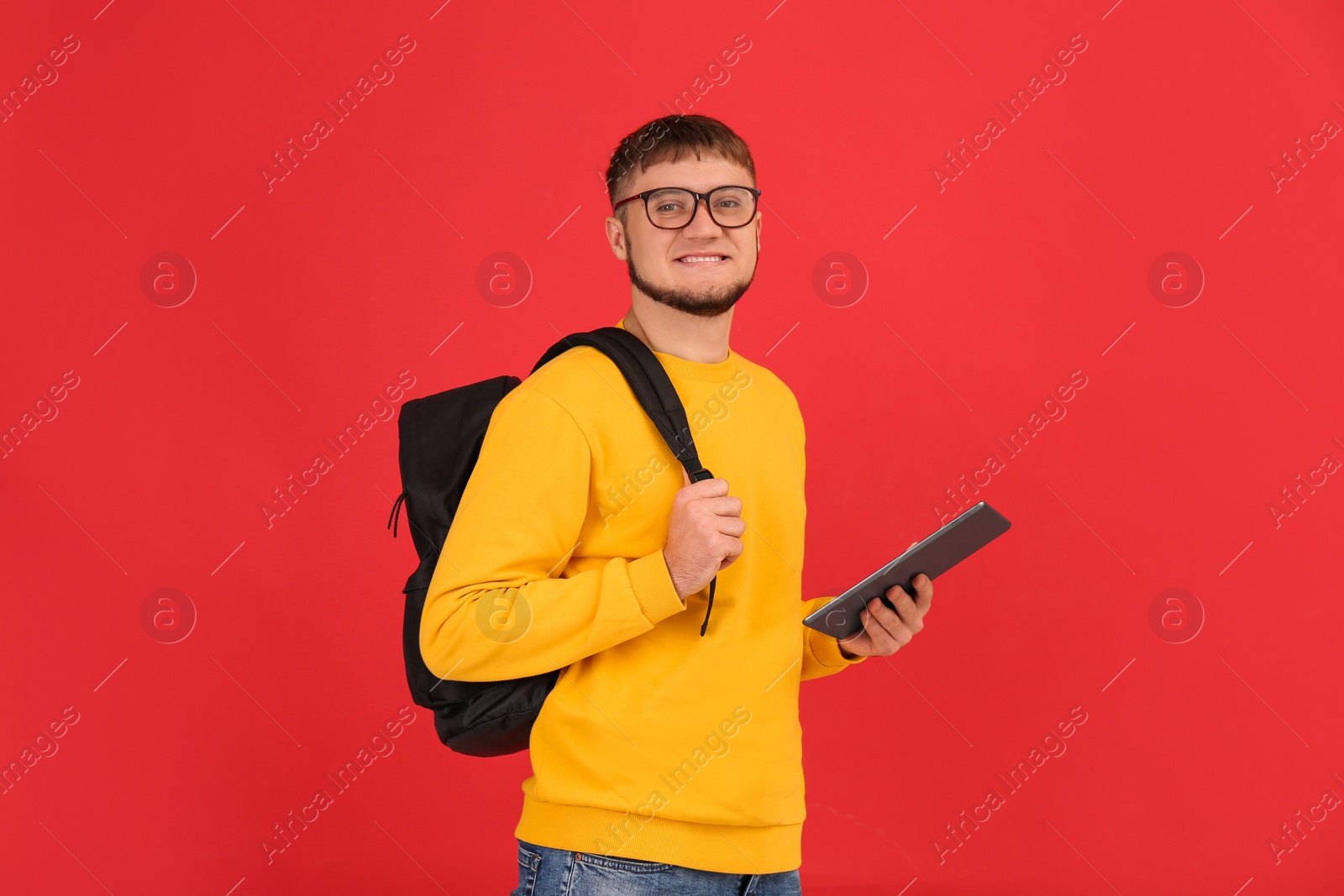 Photo of Young student with backpack and tablet on red background