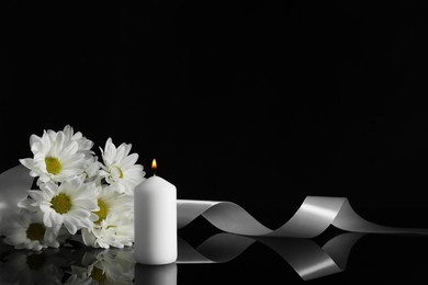 Photo of Burning candle, white chrysanthemum flowers and ribbon on black mirror surface in darkness, space for text. Funeral symbols