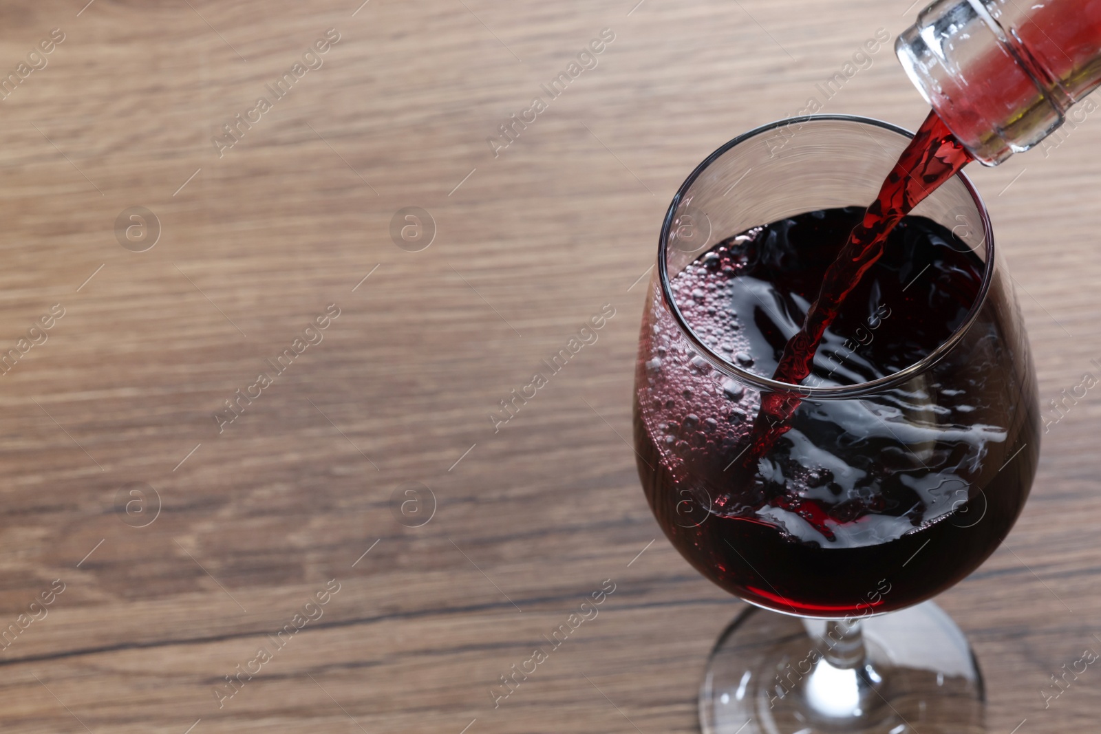 Photo of Pouring tasty red wine in glass at wooden table, closeup. Space for text