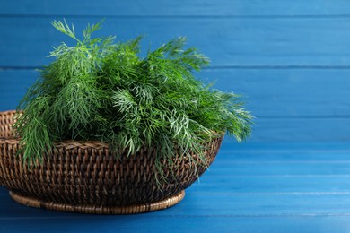 Fresh dill in wicker basket on blue wooden table, space for text