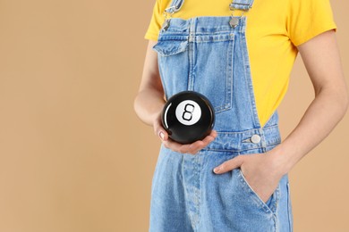 Photo of Woman holding magic eight ball on light brown background, closeup. Space for text
