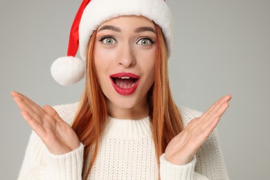 Photo of Emotional young woman in Santa hat on light grey background. Christmas celebration