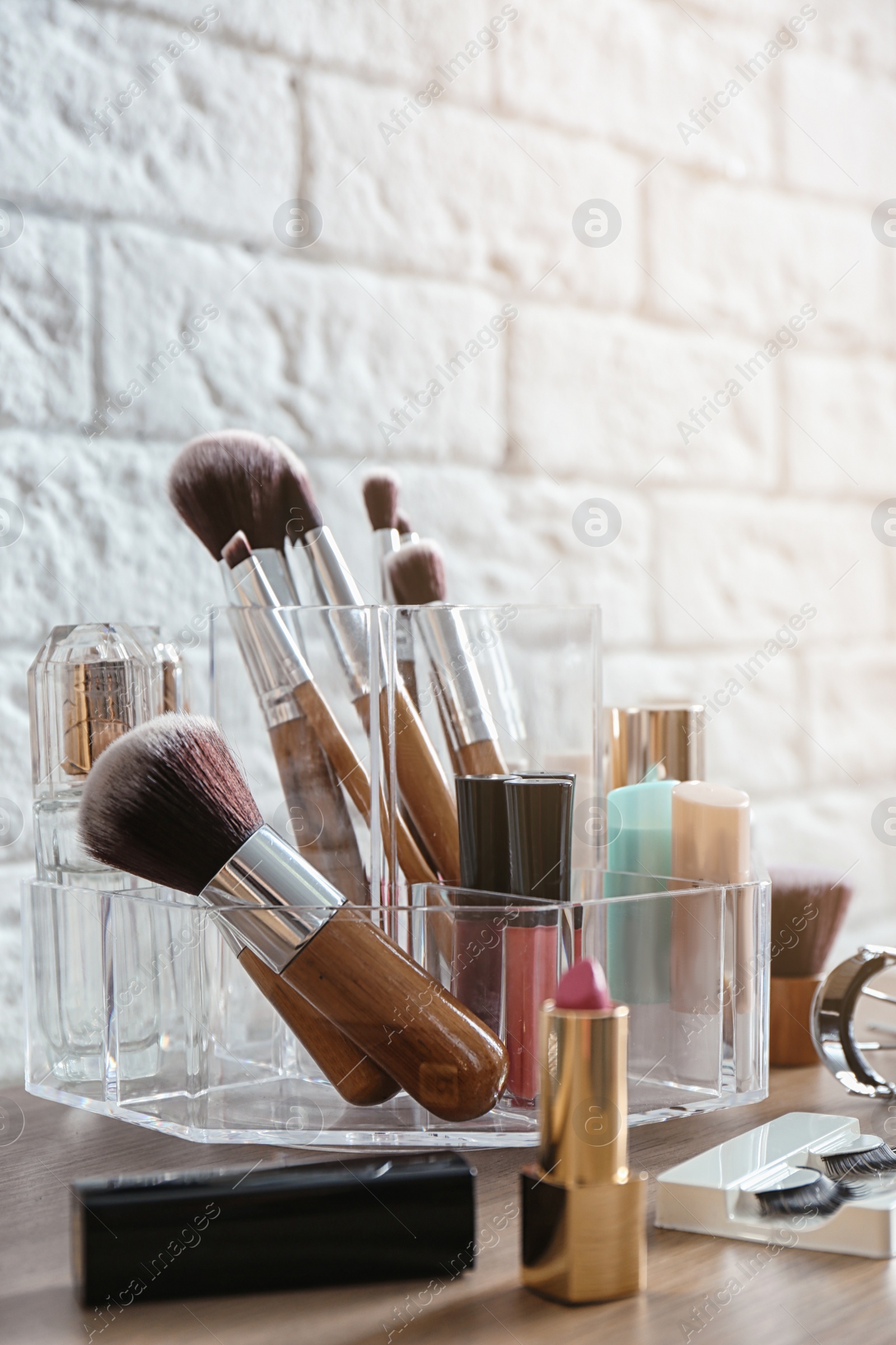 Photo of Organizer with cosmetic products for makeup on table near brick wall