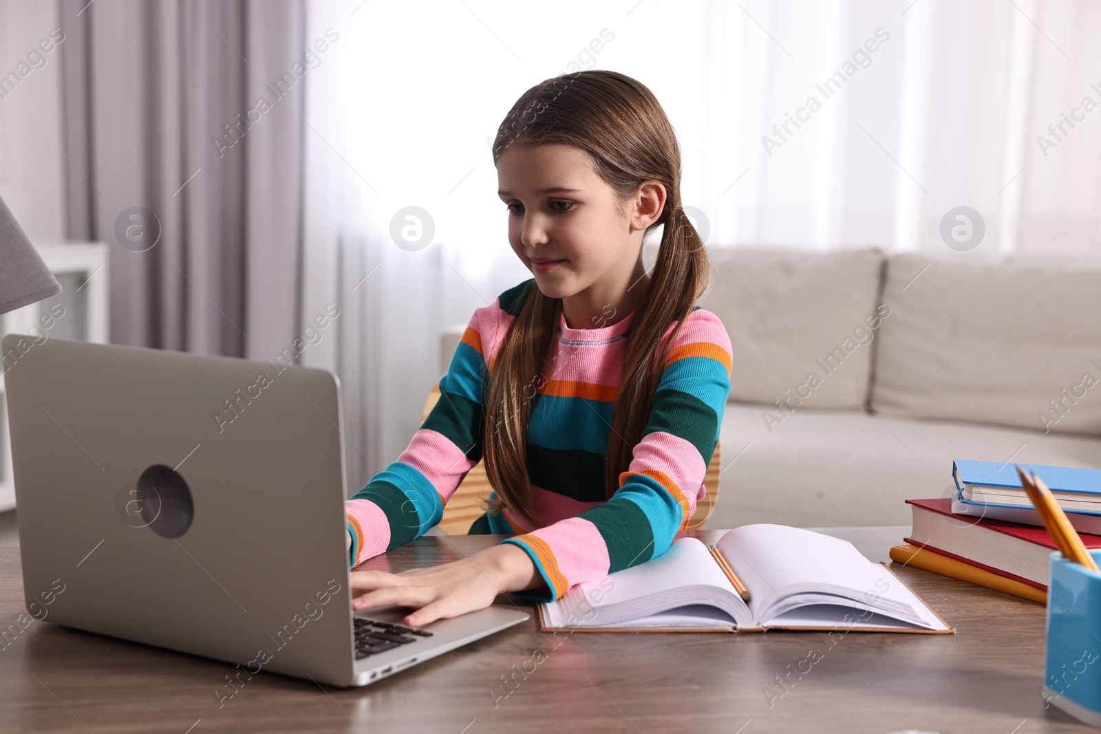 Photo of E-learning. Cute girl using laptop during online lesson at table indoors