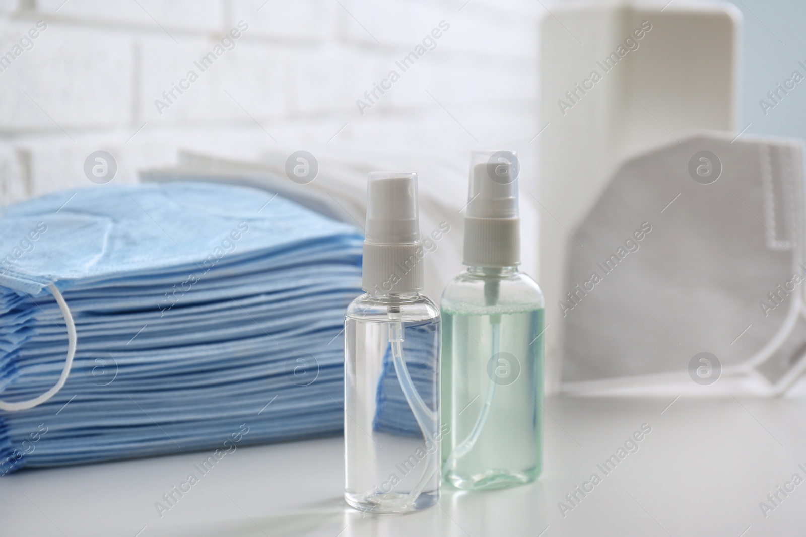 Photo of Hand sanitizers and respiratory masks on white table indoors. Protective essentials during COVID-19 pandemic