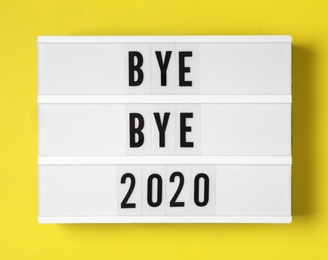Photo of Lightbox with phrase Bye Bye 2020 on yellow background, top view