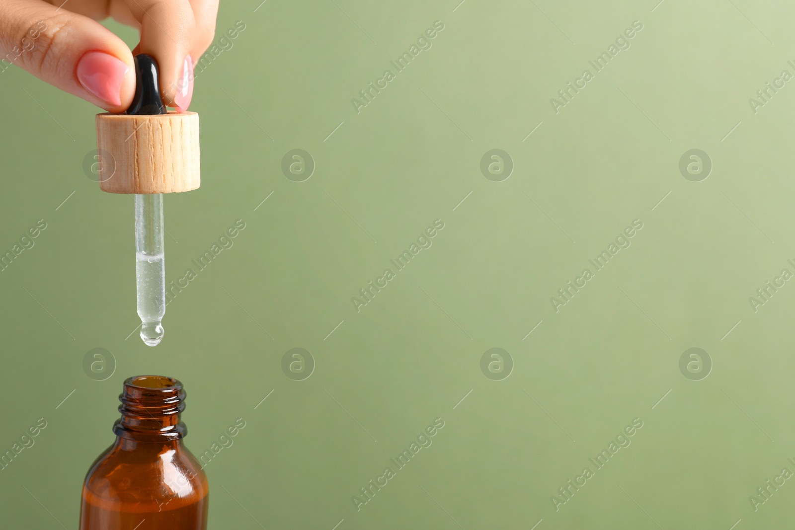 Photo of Woman dripping serum from pipette into bottle against olive background, closeup. Space for text