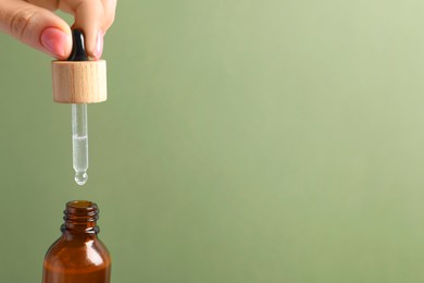 Photo of Woman dripping serum from pipette into bottle against olive background, closeup. Space for text