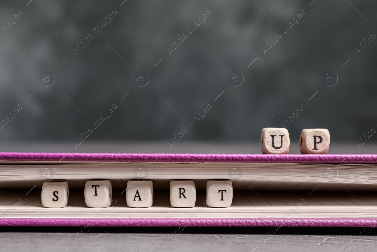 Photo of Wooden cubes with phrase Start Up and notebook on grey table, closeup. Space for text