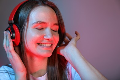 Portrait of beautiful woman with headphones on color background, space for text