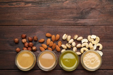 Photo of Different types of delicious nut butters and ingredients on wooden table, flat lay. Space for text