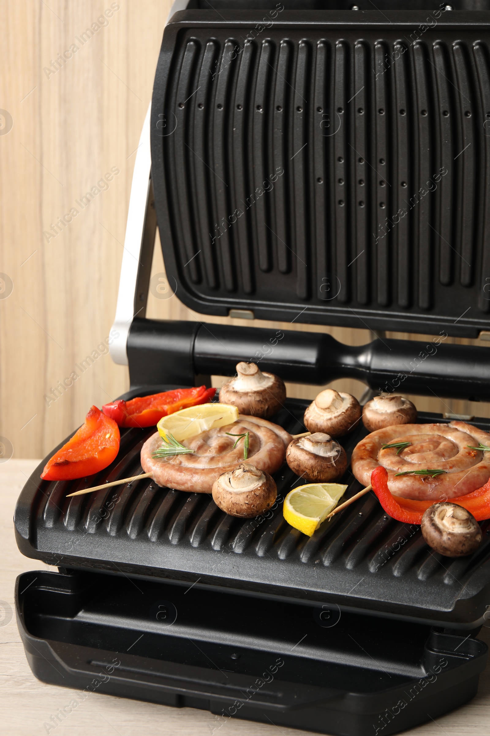 Photo of Electric grill with homemade sausages, mushrooms and bell pepper on wooden table