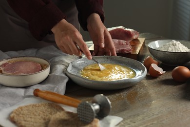 Woman cooking schnitzel at wooden table indoors, closeup