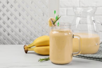 Photo of Mason jar and jug of tasty banana smoothie with fresh fruits on white marble table. Space for text