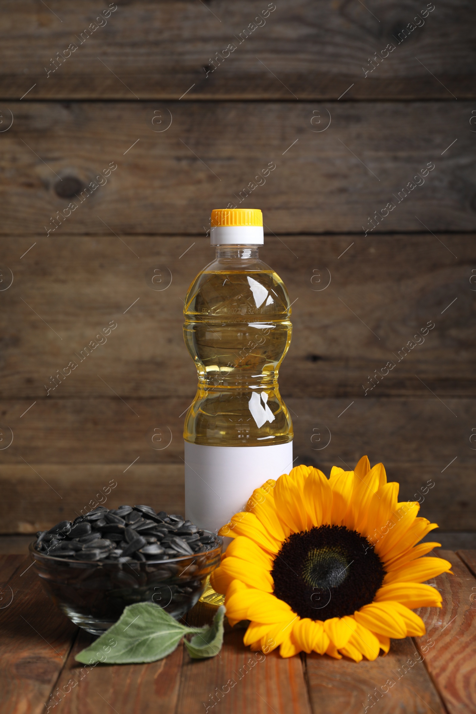 Photo of Sunflower cooking oil, seeds and yellow flower on wooden table