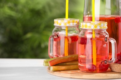 Photo of Tasty rhubarb cocktail with raspberry and stalks on white wooden table outdoors, space for text