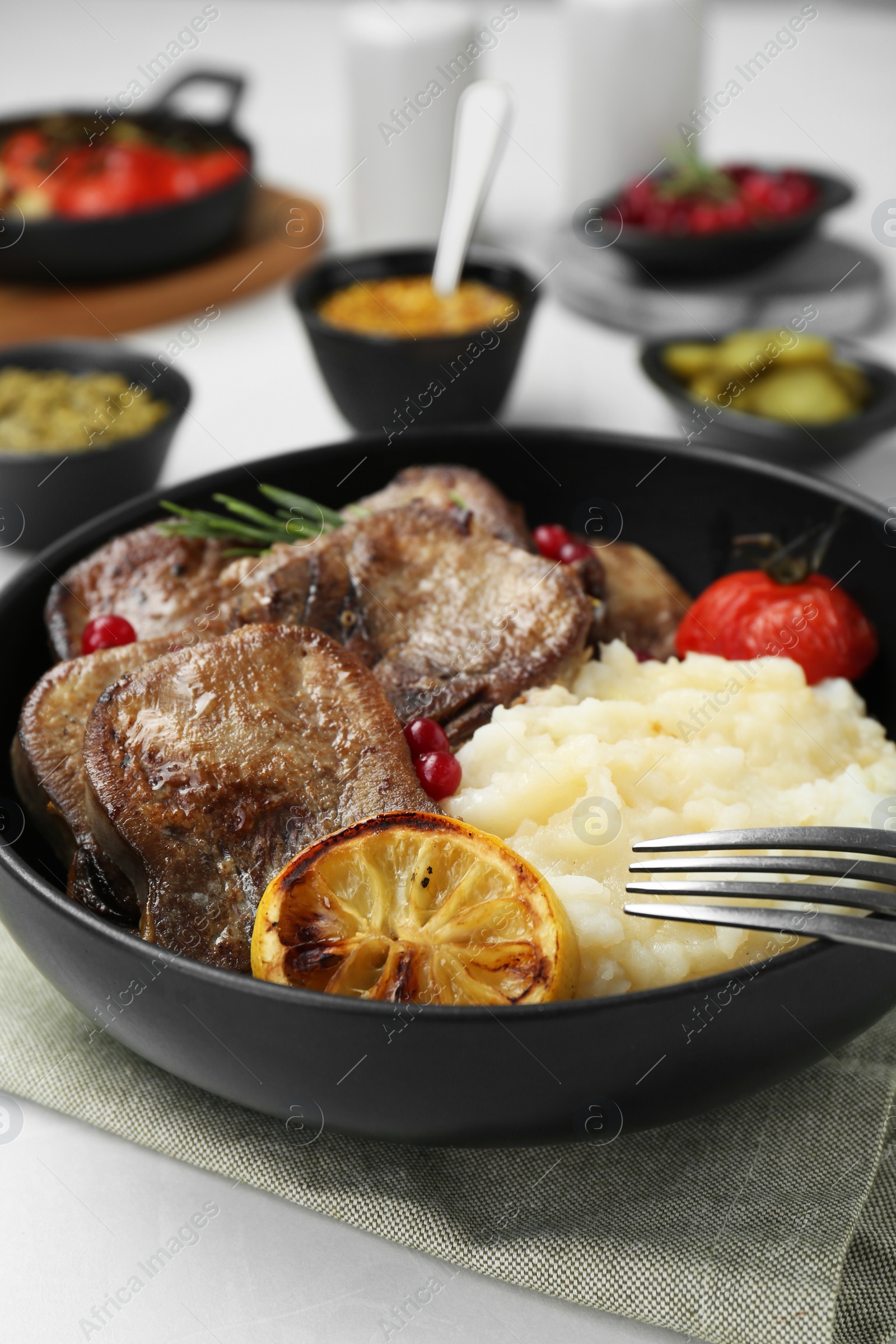 Photo of Tasty beef tongue pieces, berries, lemon, rosemary, tomato and mashed potatoes on white table, closeup