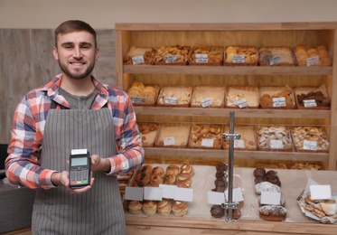 Smiling seller holding payment terminal in bakery. Space for text