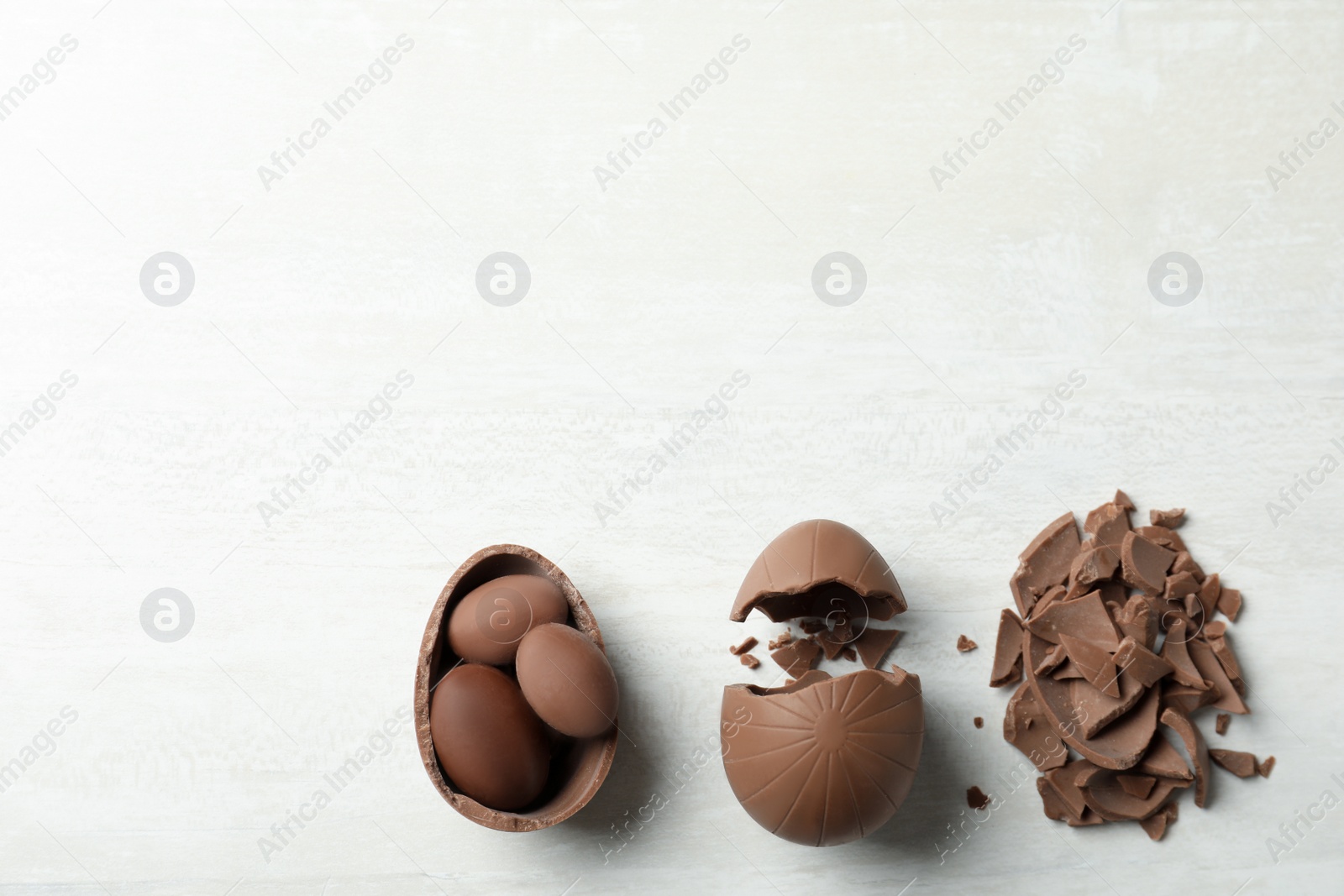 Photo of Broken chocolate eggs on white wooden table, flat lay. Space for text