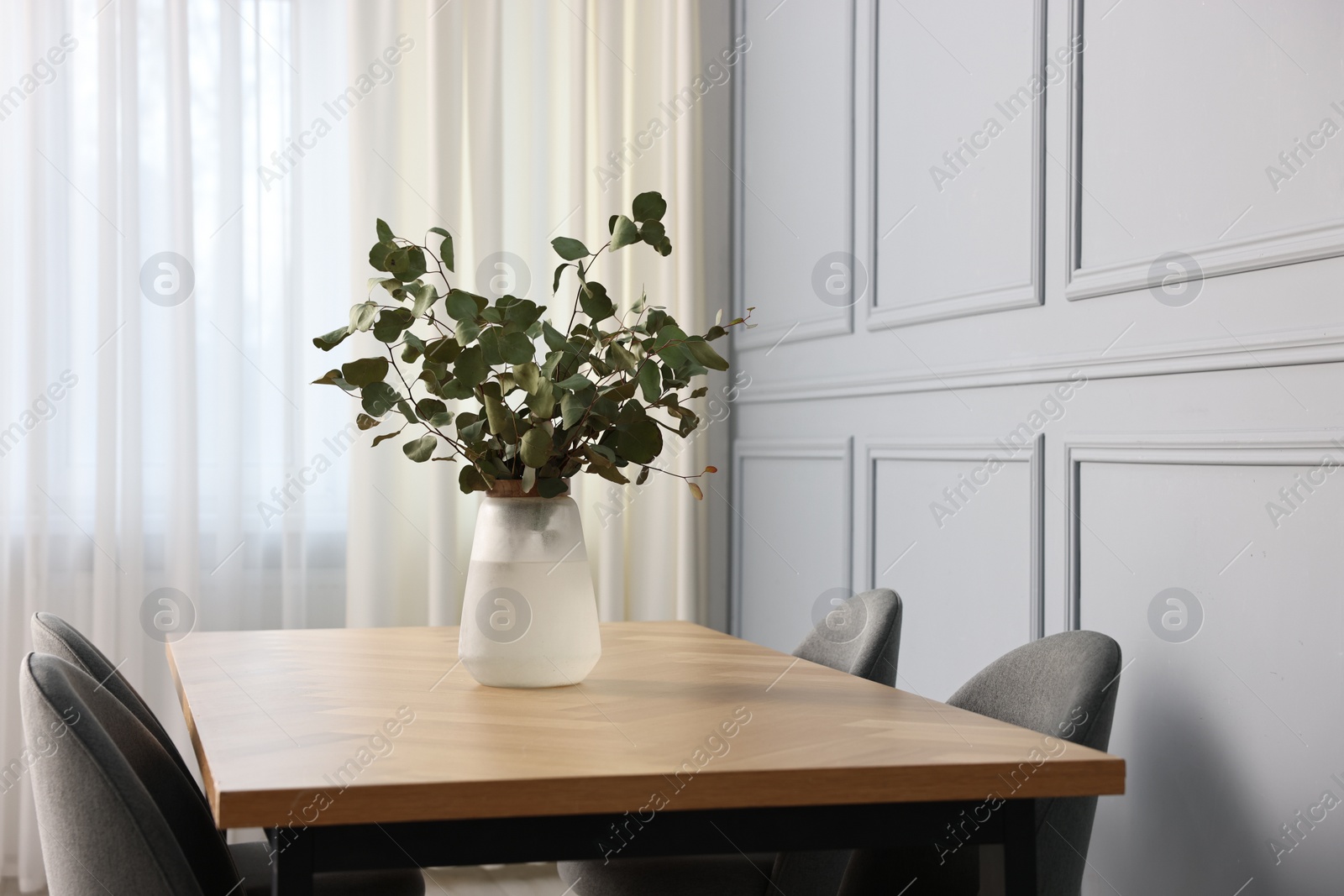 Photo of Vase with eucalyptus branches on wooden table in stylish dining room