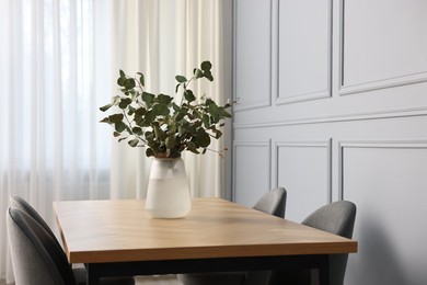 Photo of Vase with eucalyptus branches on wooden table in stylish dining room