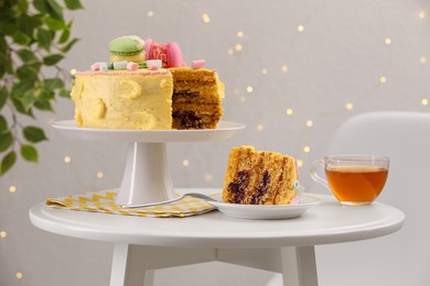 Delicious cake and tea served on white table against blurred lights