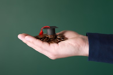 Photo of Man holding coins and graduation cap against green background, closeup. Scholarship concept