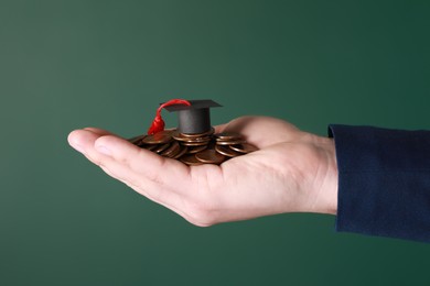 Man holding coins and graduation cap against green background, closeup. Scholarship concept