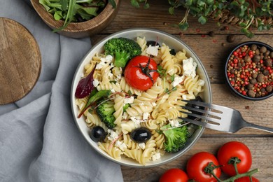 Photo of Bowl of delicious pasta with tomatoes, olives and broccoli on wooden table, flat lay