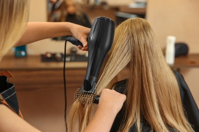 Professional hairdresser drying girl's hair in beauty salon, closeup