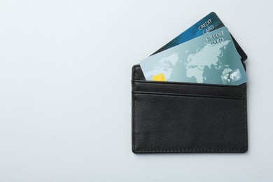 Woman holding leather card holder with credit cards on light grey background, top view. Space for text