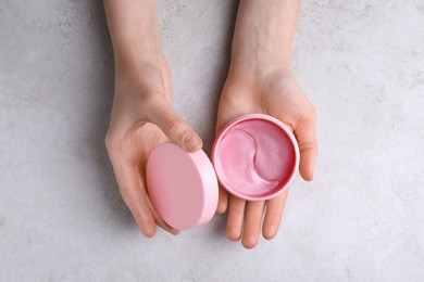 Photo of Woman holding package of under eye patches at light table, top view. Cosmetic product