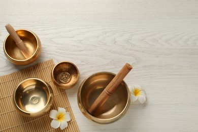 Photo of Flat lay composition with golden singing bowls on white wooden table. Space for text