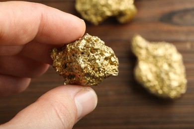 Photo of Woman holding gold nugget at wooden table, closeup. Space for text
