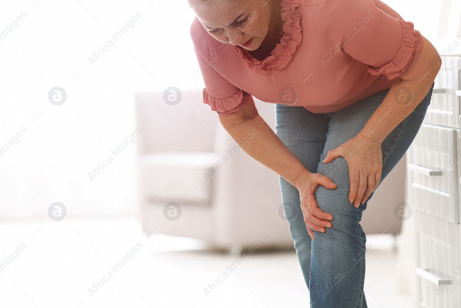 Photo of Senior woman suffering from knee pain in kitchen. Space for text